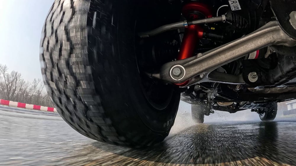 Low-mounted camera view of a truck tyre and suspension running over a wet test track