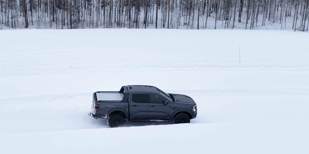 Grey Ford Ranger Raptor driving across a snow-covered test course beside a forest